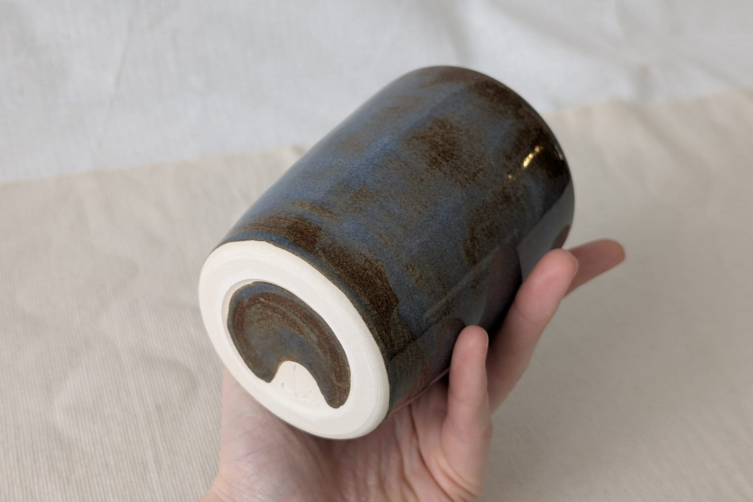 Hand holding a ceramic vase with a textured surface against a neutral background